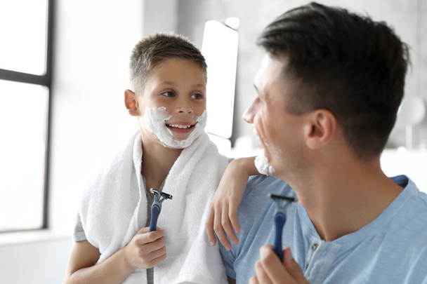 Happy father and son with shaving foam on their faces in bathroom - Фото, зображення