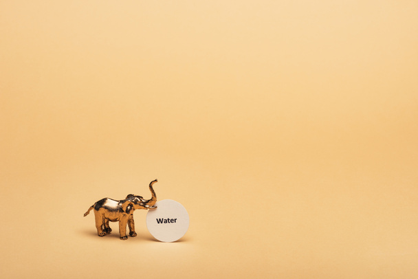 黄色の背景にカード上の文字の水と黄金のおもちゃの象、水不足の概念 - 写真・画像