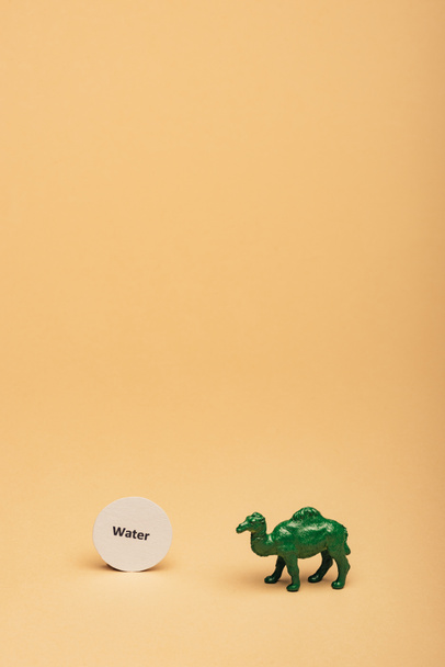 grünes Spielzeugkamel mit Schriftzug Wasser auf Karte auf gelbem Hintergrund, Wasserknappheitskonzept - Foto, Bild