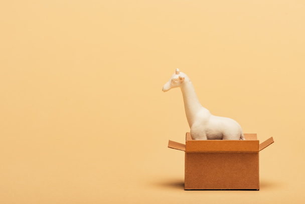 White toy giraffe in cardboard box on yellow background, animal welfare concept - Photo, Image