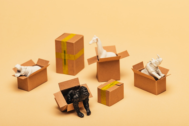 Selective focus of animal toys in cardboard boxes on yellow background, animal welfare concept - Photo, Image