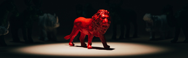 Panoramaaufnahme eines roten Spielzeuglöwen im Scheinwerferlicht mit Tieren im Hintergrund, Abstimmungskonzept - Foto, Bild