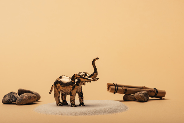 Elefante de brinquedo na areia com pedras e paus de madeira no fundo amarelo, conceito de bem-estar animal
 - Foto, Imagem