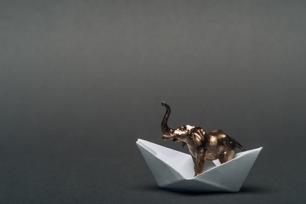 Éléphant jouet doré dans un bateau en papier sur fond gris, concept de bien-être animal
 - Photo, image