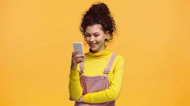 happy girl using smartphone isolated on orange  - Materiał filmowy, wideo