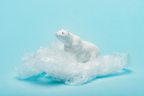 Toy polar bear on plastic packet on blue background, environmental pollution concept - Foto, imagen