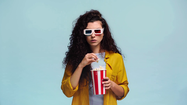 scared girl in 3d glasses eating popcorn isolated on blue  - Footage, Video