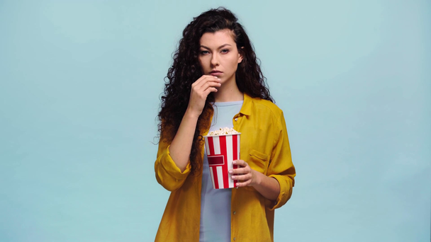 young woman eating popcorn isolated on blue  - Felvétel, videó