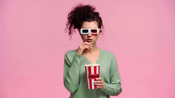 φοβισμένο κορίτσι σε 3d ποτήρια τρώει ποπ κορν απομονωμένο σε ροζ  - Πλάνα, βίντεο