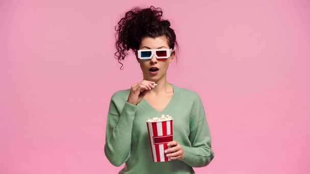 surprised girl in 3d glasses eating popcorn isolated on pink  - Πλάνα, βίντεο