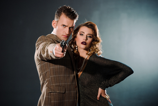 selective focus of dangerous gangster holding gun and standing near attractive woman  on black  - Zdjęcie, obraz