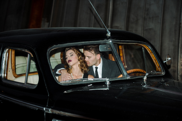 handsome gangster sitting in retro car with woman  - 写真・画像