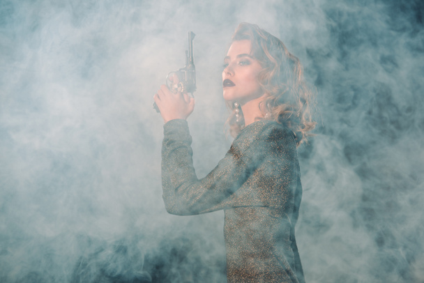 煙の近くで銃を持っている魅力的で危険な女性  - 写真・画像