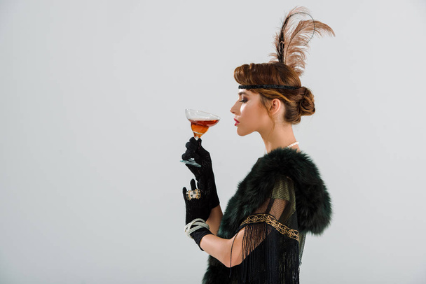 vista laterale della donna attraente ed elegante che tiene il vetro con bevanda alcolica isolata sul grigio
  - Foto, immagini