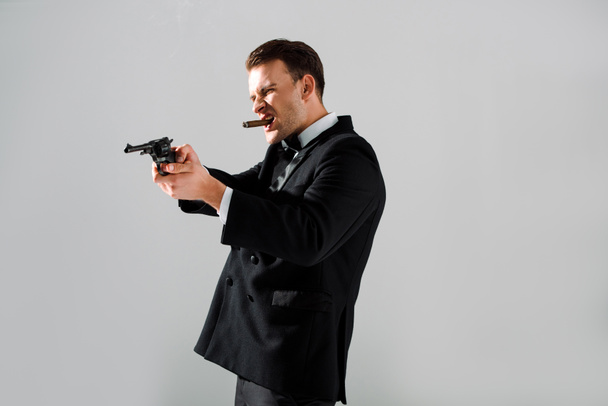 guapo gangster sosteniendo pistola mientras fumar aislado en gris
  - Foto, imagen