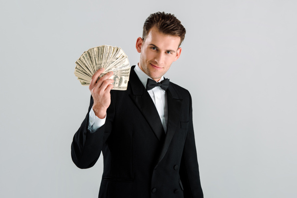 happy and rich man in suit holding dollar banknotes isolated on grey  - Foto, afbeelding