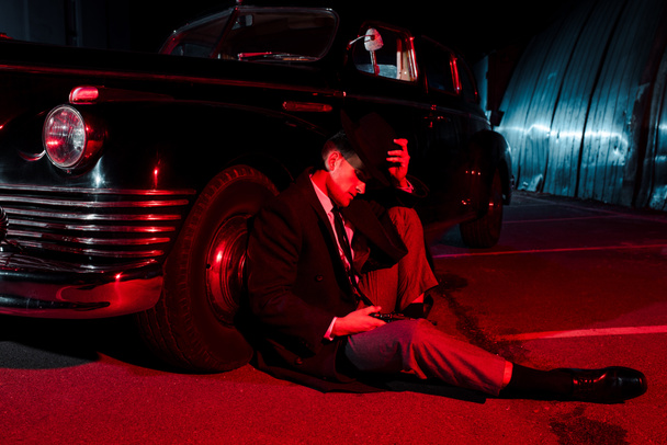 elegante gángster usando sombrero mientras está sentado cerca de coche retro
  - Foto, imagen