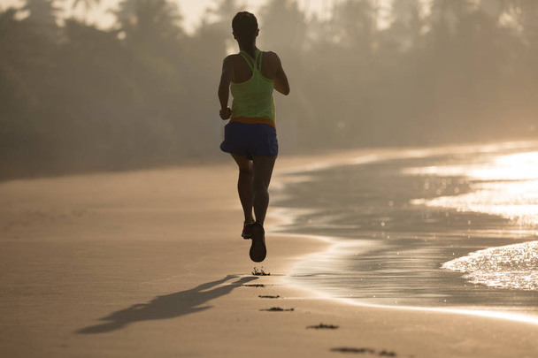 Fitness woman running on sunrise beach - Foto, afbeelding