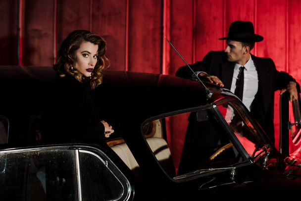 selective focus of attractive woman standing near retro car and man in hat  - Photo, Image