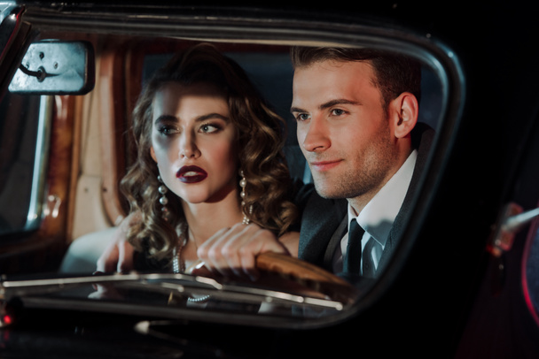 selektywne skupienie szczęśliwy mężczyzna dotykając kierownicy i siedzi w pobliżu atrakcyjnej kobiety w samochodzie retro  - Zdjęcie, obraz