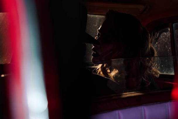 selective focus of attractive woman near man in hat sitting in retro car  - Zdjęcie, obraz