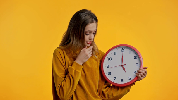 senny nastolatek trzymając zegar izolowany na żółty - Materiał filmowy, wideo