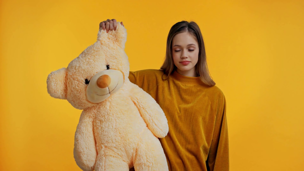 teenager holding teddy bear isolated on yellow - Záběry, video