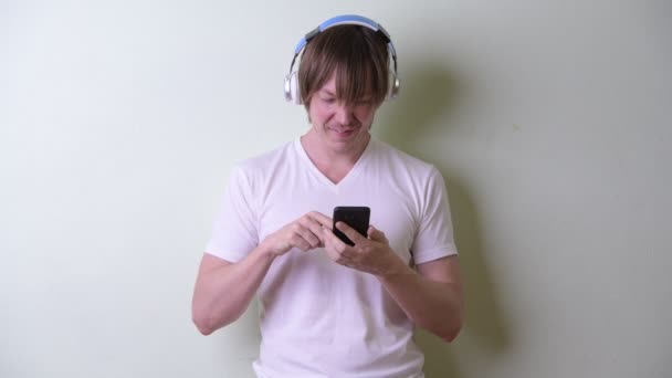 Happy young man with long hair using phone and listening to music - Metraje, vídeo