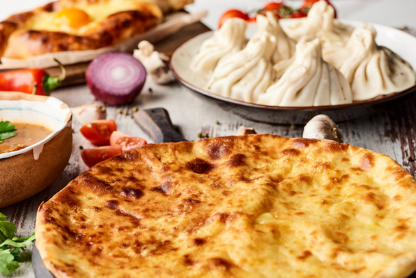 selective focus of Imeretian and Adjarian khachapuri, kharcho and khinkali on wooden table - Photo, Image
