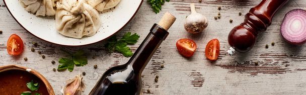 вид сверху на вкусный хинкали возле бутылки вина, харчо, овощи и специи на деревянном столе, панорамный снимок
 - Фото, изображение