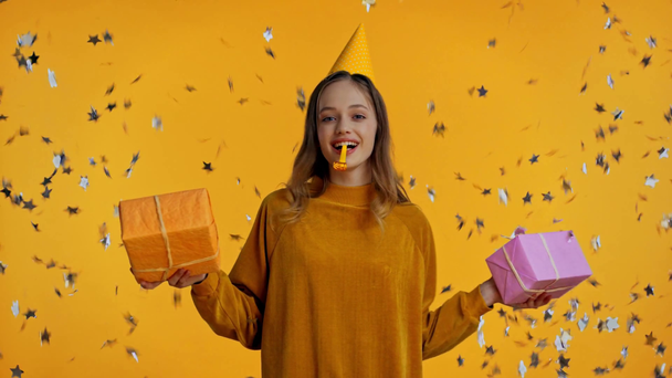 teenager držení dárky a troubení v party rohu izolované na žluté - Záběry, video