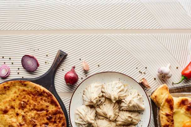 top view of delicious khinkali and khachapuri near vegetables and spices on beige textured background - Foto, immagini