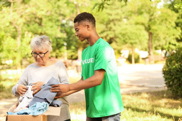 Giovane afro-americano volontario dando nuovi vestiti per la povera donna anziana all'aperto
 - Foto, immagini