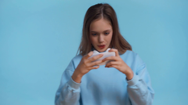Teenager spielt mit Smartphone isoliert auf blauem Grund - Filmmaterial, Video