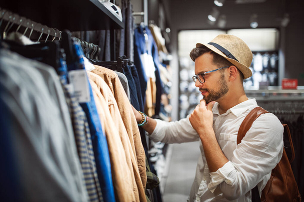 Handsome young man shopping for new clothes in store - 写真・画像