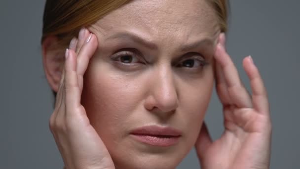 Upset woman massaging temples and looking at camera, migraine pain, head ache - Felvétel, videó