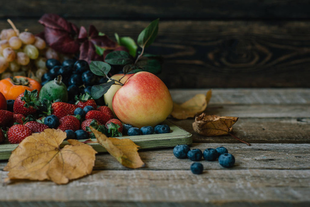 Vintage wooden tray and fresh fruits on wooden table. Fresh organic fruits and fall leaves. Autnum harvest. Toned vintage image with copy space. - Fotó, kép