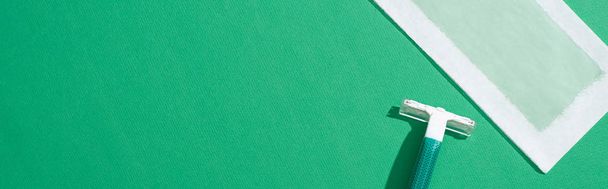 vista superior da navalha descartável verde e tarja de cera de depilação no fundo verde, tiro panorâmico
 - Foto, Imagem