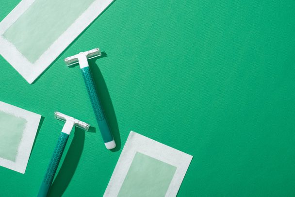 vista superior de lâminas descartáveis verdes e listras de cera de depilação no fundo verde
 - Foto, Imagem