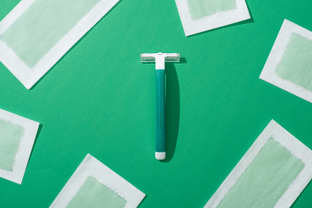 felülnézet zöld eldobható borotva és szőrtelenítés viasz csíkok zöld háttér - Fotó, kép