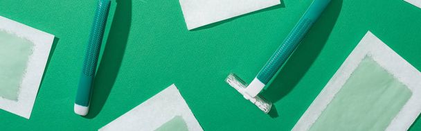 bovenaanzicht van groene wegwerp scheermessen en ontharing wax strepen op groene achtergrond, panoramisch schot - Foto, afbeelding