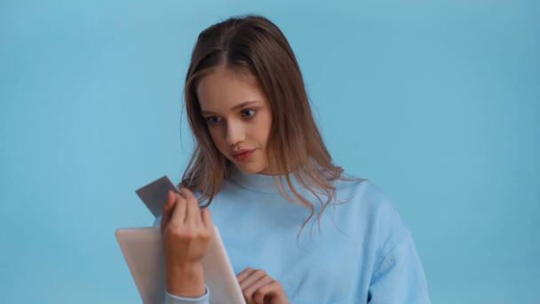 Teenager benutzt Gadget und hält Kreditkarte isoliert auf blauem Grund - Filmmaterial, Video