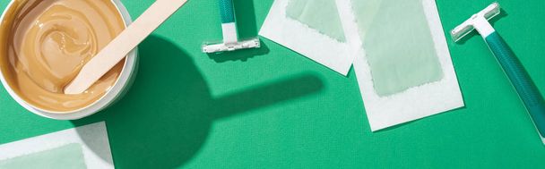 top view of green disposable razors, wax and depilation stripes on green background, panoramic shot - Photo, Image