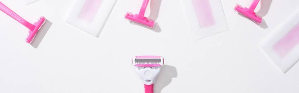 vista superior de maquinillas de afeitar de color rosa y rayas de cera depilación sobre fondo blanco, plano panorámico
 - Foto, imagen
