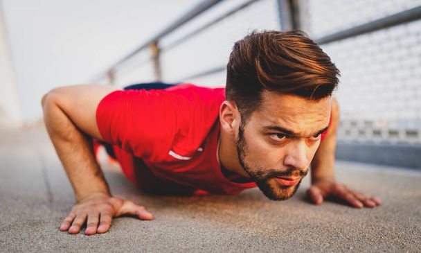 Beautiful fit male runner stretching before workout, fit man doing exercises outdoors - Fotoğraf, Görsel
