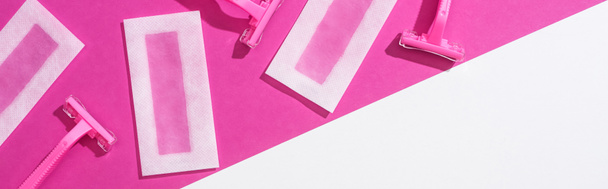 bovenaanzicht van wegwerp scheermessen en wax ontharingsstrepen op witte en roze achtergrond, panoramisch schot - Foto, afbeelding