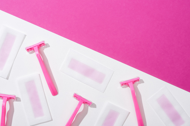 bovenaanzicht van wegwerp scheermessen en wax ontharingsstrepen op witte en roze achtergrond - Foto, afbeelding