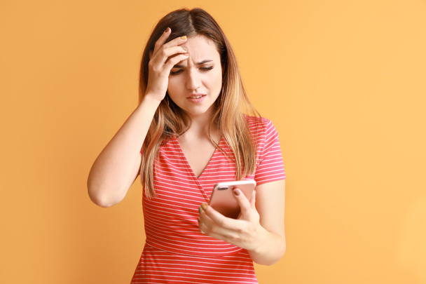 Portrait of worried young woman with mobile phone on color background - Fotó, kép