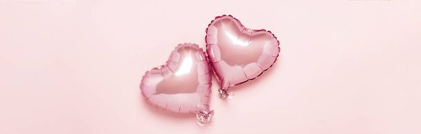 Two pink air balloons in the shape of a heart on a pink background. Concept Valentine's Day, Wedding Decoration. Foil balls. Banner. Flat lay, top view - Photo, image