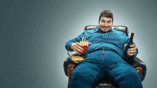 Fat man sitting in a brown armchair, emotional watching TV - Fotó, kép